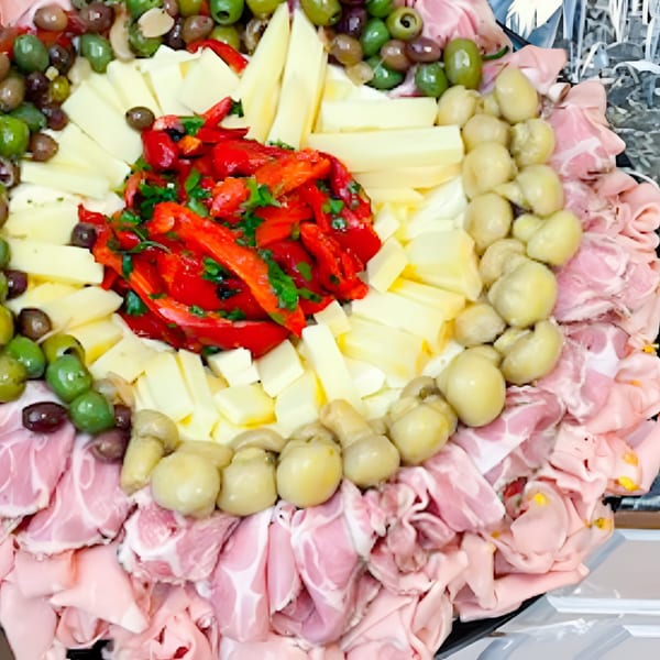 A deli platter with cured meats, cheeses, olives, marinated mushrooms, and roasted red peppers.