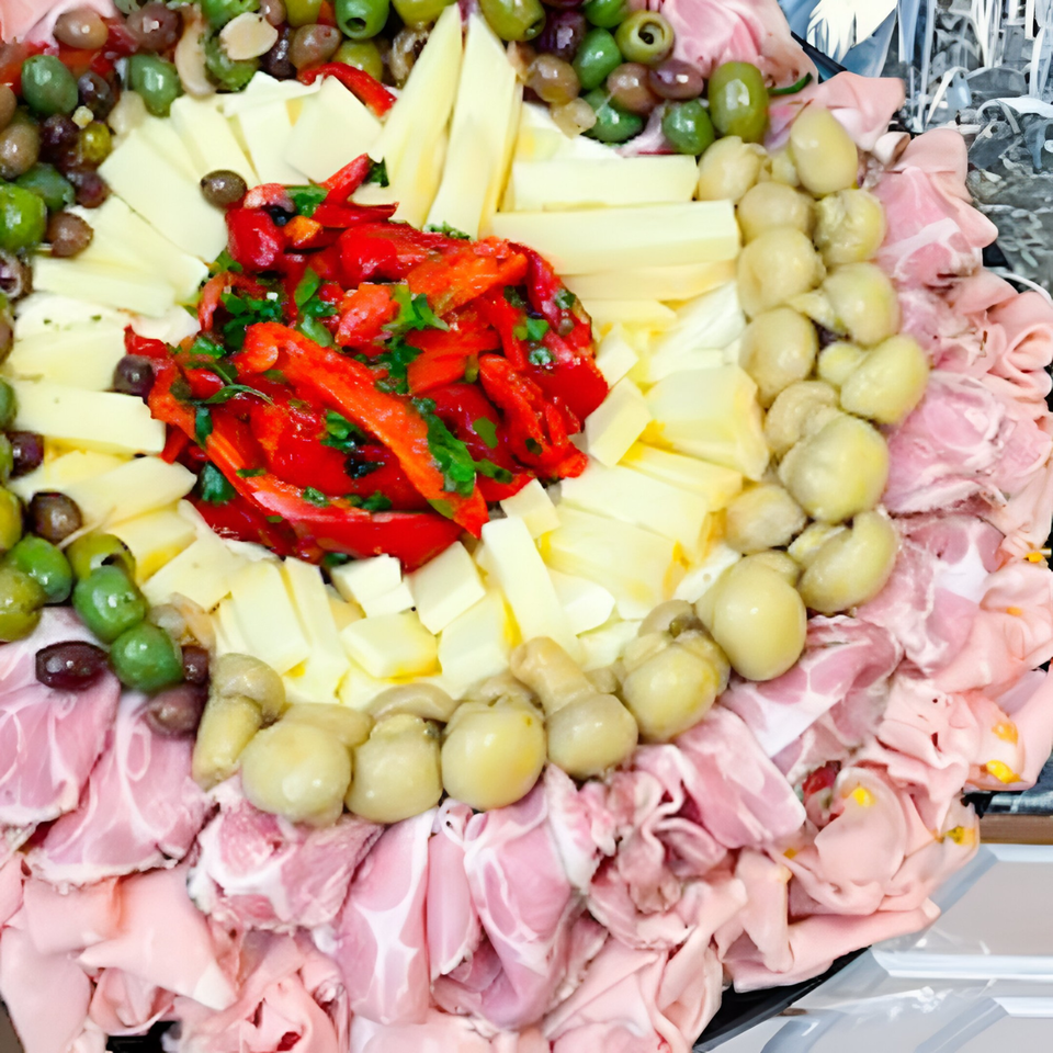 A deli platter with cured meats, cheeses, olives, marinated mushrooms, and roasted red peppers.