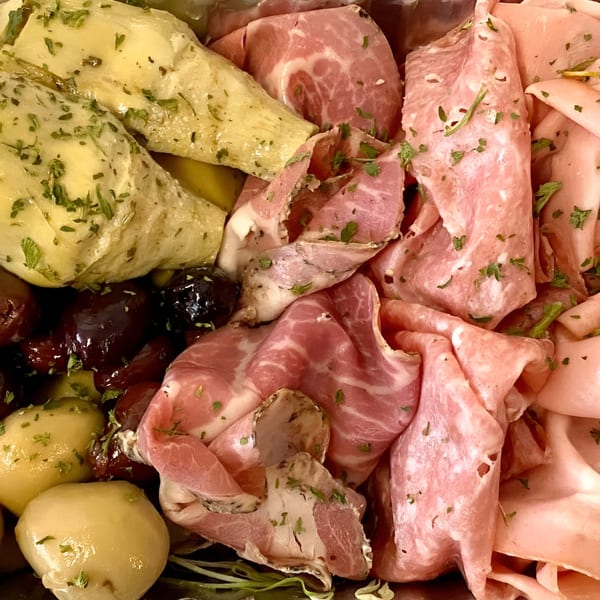 Close-up of a deli platter with sliced meats, marinated artichokes, olives, and small potatoes.