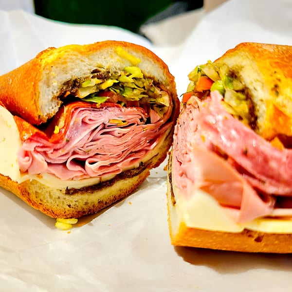 A Neapolitan Gourmet deli sandwich, sliced in half, revealing layers of meat, cheese, and vegetables.