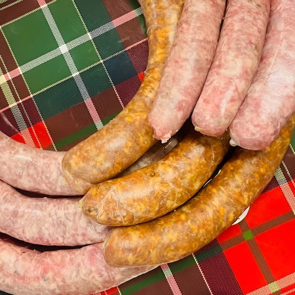 Two types of raw sausages, light pink and golden brown, arranged on a red and green plaid tablecloth.
