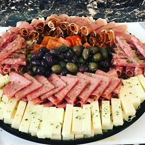 A deli platter with rolled meats, salami, olives, and cheese sticks, garnished with herbs.