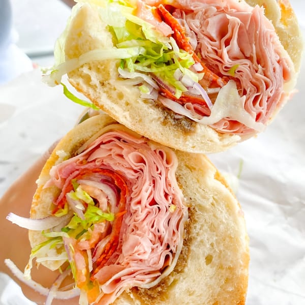 A Neapolitan Gourmet deli sandwich, cut in half, filled with meats, cheese, lettuce, and onions.