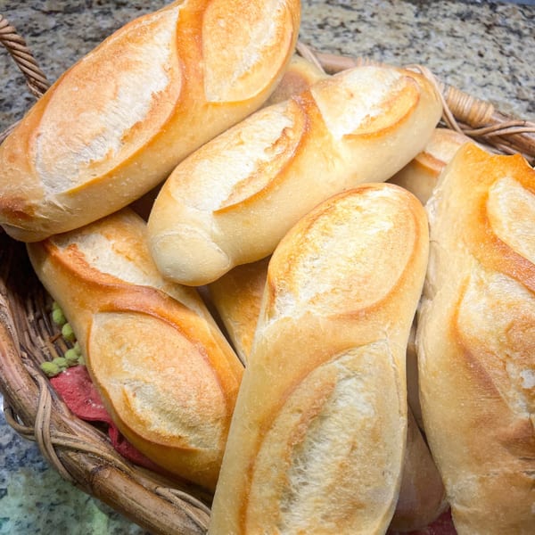 Freshly baked, golden-crusted bread rolls, likely for sandwiches, fill a rustic woven basket.