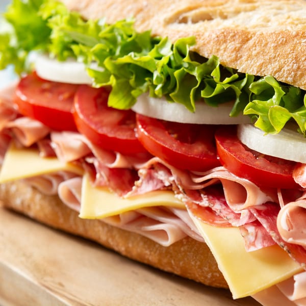 Close-up of a Neapolitan Gourmet deli sandwich with meat, cheese, lettuce, tomatoes, and onions.